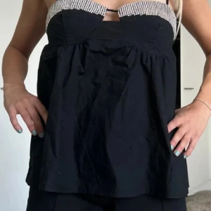 Svart bandeau topp med strass från Zara - Supersnygg svart bandeau topp från Zara med glittriga strassdetaljer upptill och öppen rygg. Toppen har en luftig och lös passform med tunna axelband och är perfekt för att sticka ut. Materialet känns lätt och bekvämt.