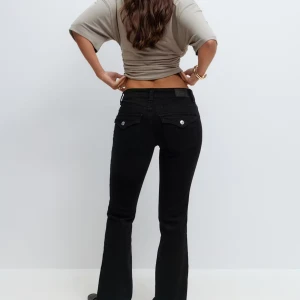 Svarta bootcut jeans med fickdetaljer - Snygga svarta jeans med bootcut passform och klassiska fickor med lock och silverknappar bak. Jeansen har låg midja och är tillverkade i stretchigt denim för en bekväm känsla. Perfekta för dig som gillar en tidlös och clean look. Helt nya, oanvända från Gina kostar normalt 500kr säljer halva priset 