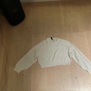 Vit croppad stickad tröja H&M XS - Säljer en vit croppad stickad tröja från H&M i storlek XS. Tröjan har ett snyggt hålmönster och ribbade muddar vid ärmslut och nederkant. Perfekt för dig som gillar en fräsch och trendig look med långärmade ärmar och rund hals.