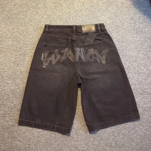 Svarta denimshorts från SumwonStudios - Säljer ett par svarta jeans denimshorts från SumwonStudio med loose passform och midwaist. Baksidan har coolt graffiti-tryck över bakfickorna. Klassisk femficksdesign och silverfärgade nitar framtill. Perfekt för dig som gillar streetstyle.