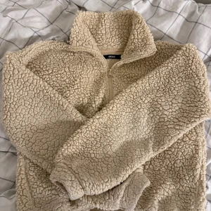 Beige fleece-tröja från Bik Bok - Supermysig beige fleece-tröja från Bik Bok med halv dragkedja och hög krage. Tröjan har långärmade ärmar och snörning i nederkant för att justera passformen. Perfekt för kalla dagar när du vill vara både varm och chill. 