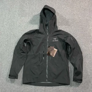 Svart Arc'teryx vindjacka med huva - Säljer en svart vindjacka från Arc'teryx med huva och dragkedja framtill. Jackan har flera fickor med dragkedja och justerbara ärmslut. Perfekt för dig som gillar stilren och funktionell design. Logga på bröstet och diskret look.