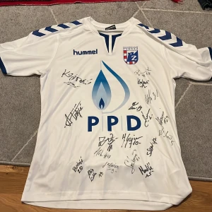 Vit Zagreb fotbollströja Hummel S - Säljer en vit handbollströja från Hummel, officiell Zagreb-klubbtröja i storlek S (EU). Tröjan har blå detaljer, tryck med PPD och klubbmärke på bröstet samt autografer från spelare. Materialet är lätt och andas, perfekt för träning eller match. 