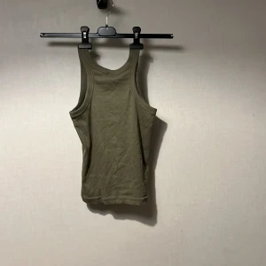 Olivgrön linnetopp från Kappahl - Snygg olivgrön linnetopp från Kappahl i storlek 158/164. Modellen är klassisk med breda axelband och rundad halsringning. Materialet är mjuk bomull som känns skönt mot huden. Perfekt för dig som gillar enkel och stilren look.