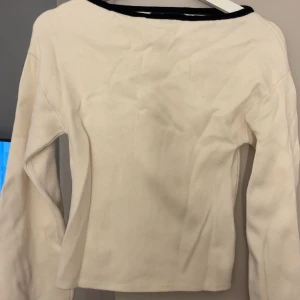 Vit långärmad tröja Gina Tricot XS - En stilren vit långärmad tröja från Gina Tricot i storlek XS. Tröjan har en enkel design med svarta detaljer vid halsringningen och är tillverkad i ett mjukt bomullsmaterial. Perfekt för en clean och klassisk look.