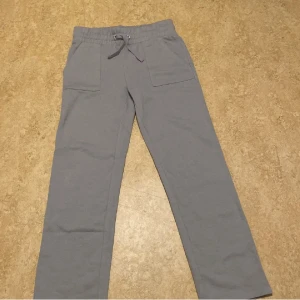 Grå mjukisbyxor med snörning - Grå mjukisbyxor med raka ben, resår och snörning i midjan. Byxorna har stora fickor fram och bak, och är tillverkade i mjukt bomullsmaterial. Perfekta för en chill och avslappnad stil.