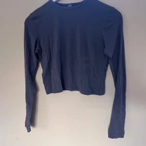 Mörkblå croppad långärmad topp från Skims - Säljer en stilren mörkblå croppad topp från Skims med lång ärm och rund hals. Toppen är tillverkad i mjuk bomull med lite stretch för skön passform. Perfekt att matcha med jeans eller kjol för en chill look.