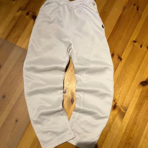 Vita mjukisbyxor från Polo Ralph Lauren - Snygga vita mjukisbyxor från Polo Ralph Lauren med klassisk broderad logga i svart på höften. Byxorna har elastisk midja och är tillverkade i mjukt bomullsmaterial för maximal komfort. Perfekta för chill dagar eller när du vill ha en clean och enkel look.