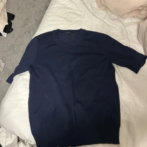 Mörkblå stickad kortärmad tröja - En stilren mörkblå stickad tröja med rund halsringning och korta ärmar. Perfekt för dig som gillar en enkel men snygg look. Tröjan har en mjuk känsla och passar bra till både jeans och kjol.