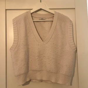 Vit stickad väst från Gina Tricot - Snygg vit stickad väst från Gina Tricot med bred ribbad kant vid ärmhål och nederkant. Västen har en djup v-ringning och är perfekt för att styla över en skjorta eller t-shirt för en chill look.