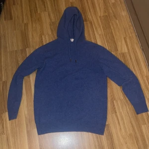 Blå stickad hoodie med huva - Mysig blå hoodie i stickat material med huva och snörning. Tröjan har långärmade ärmar och en enkel, clean look utan mönster eller logga. Perfekt för dig som gillar chill och stilren vibe.