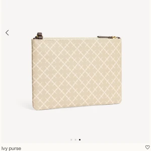 Beige kuvertväska från By Malene Birger - Snygg beige kuvertväska med rutigt mönster från By Malene Birger. Väskan har en smal brun axelrem och guldfärgad dragkedja. Tillverkad i syntetmaterial med stilren design och praktisk storlek för det viktigaste.