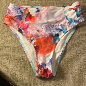 Färgglad bikiniunderdel med hög midja 36 mkt fin  - Säljer ett par bikiniunderdelar med hög midja i ett färgstarkt, abstrakt mönster med inslag av rosa, blått, lila, rött och vitt. Materialet är mjukt och stretchigt, perfekt för strand eller pool. Sitter snyggt och ger en modern vibe till din badoutfit. 36. Stadium. Inga fläckar 
