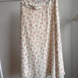 Blommig kjol från NAKD - Söt, midilång kjol från NA-KD med små rosa och grå blommor på. Dold dragkedja på vänster sida. Storlek 36. Använt ett par gånger, är i mycket bra skick.