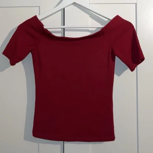 Vinröd offshoulder topp - Snygg vinröd topp med offshoulder-design och korta ärmar. Modellen är tight och har en enkel, stilren look utan mönster eller detaljer. Perfekt för dig som gillar minimalistisk stil och vill ha en topp som sitter snyggt på kroppen.