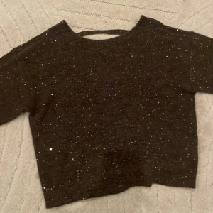 Svart glittrig stickad tröja Gina Tricot - Svart stickad tröja från Gina Tricot med glittriga paljetter över hela tröjan. Tröjan har rund halsringning och långa ärmar. Perfekt för dig som vill ha något extra snyggt och mysigt i garderoben. Tröjan är även lite öppen i ryggen. 