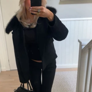 Svart pälsjacka från Neo Noir - Säljer en svart pälsjacka från NOIR med fluffig päls runt kragen och stora fickor framtill. Använd fåtal ggr. 