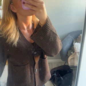 Brun stickad kofta med knappar - Mysig brun stickad kofta med v-ringning och stora knappar framtill. Koftan har två fickor och breda ribbade muddar vid ärmsluten. Perfekt för lager-på-lager och chill dagar. Använd endast en gång, säljs pga ingen användning💕