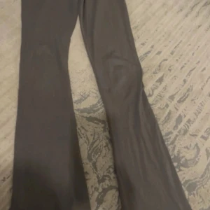 Grå bootcut byxor i stretchigt tyg - Säljer ett par gråa bootcut byxor med hög midja och tight passform upptill som släpper ut vid bensluten. Byxorna är i ett mjukt och stretchigt material som sitter snyggt och bekvämt. Perfekta för dig som gillar en clean och stilren look. Yoga pants, har aldrig haft på mig de men de är så fina verkligen