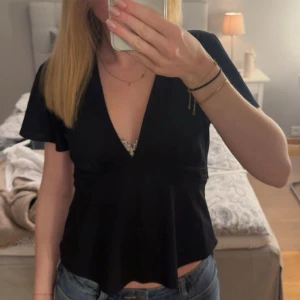 Svart v-ringad topp med knyte i ryggen - Toppen kommer från Gina Tricot och köptes i våras men är aldrig använd. Den är i storlek S och sitter väldigt fint med knytet i ryggen. Jag säljer den då jag inte hinner använda den. Hör gärna av dig vid frågor🤎