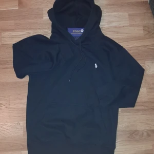 Svart hoodie från Polo Ralph Lauren - Svart hoodie från Polo Ralph Lauren med klassisk huva och snörning. Tröjan har en vit broderad logga på bröstet och en stor magficka. Tillverkad i mjuk bomull och polyesterblandning, perfekt för chill dagar. Långärmad och med ribbade muddar för extra komfort. De n är helt ny polo hoodie och jätte fin.