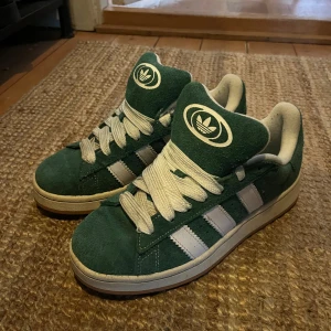 Adidas sneakers gröna mocka strl 40 - Gröna Adidas sneakers i mocka med klassiska vita ränder och logga på plös och häl. Skorna har vit sula och breda vita snören. Snygg retrostil som sticker ut och passar perfekt till streetwear. Storlek 40. Pris kan ändras det är bara att skriva och skriv för fler frågor!!