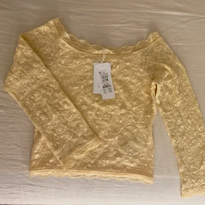 Ljusgul spets off shoulder topp - Superfin ljusgul offshoulder topp från Gina Tricot i storlek 158/164. Toppen är helspets med vacker blommig struktur och har långa ärmar. Söt spetskant runt halsringningen och nederkanten ger en extra romantisk vibe. Perfekt för dig som gillar detaljer och mjuka färger.