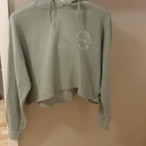 Grön croppad hoodie från Bik Bok - Snygg ljusgrön croppad hoodie från Bik Bok med tryck på bröstet 'Sports Studio'. Tröjan har huva med snörning och långa ärmar. Perfekt för en chill och avslappnad stil. Mjuk och skön bomullskänsla.