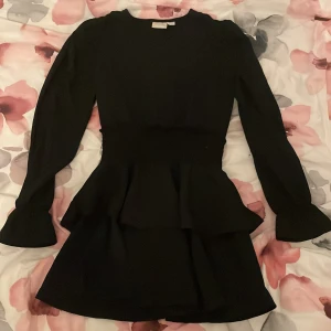 Svart volangklänning med långa ärmar - Supersnygg svart kortklänning med volangdetaljer i midjan och långa ärmar. 