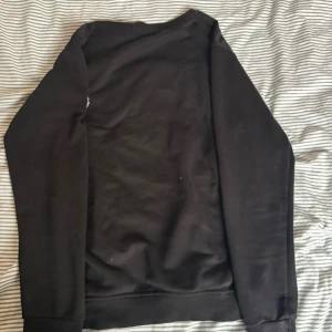 Svart sweatshirt från Moncler - Svart sweatshirt från Moncler med stort broderat Moncler-logo på bröstet och en mindre logga på ärmen. Tröjan har rund halsringning och långa ärmar. Perfekt för dig som gillar stilrena och exklusiva plagg.