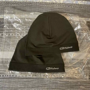 Svarta mössor från Kalenji - Två svarta mössor från Kalenji med stilren design och logga framtill. Mössorna är tunna och smidiga, perfekta för träning eller när du vill ha något enkelt på huvudet. Materialet är mjukt och stretchigt syntet som sitter skönt utan att klämma.