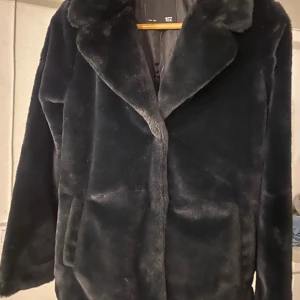 Svart pälsjacka från 157 - Säljer en svart pälsjacka från 157 med bred krage och mjuk, fluffig yta. Jackan har en klassisk rak passform och är helsvart med diskret fickor på sidorna. Perfekt för dig som vill ha en stilren och cozy look under kalla dagar.