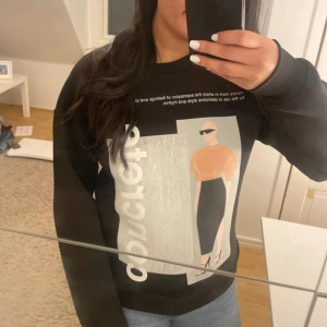 Svart sweatshirt med print från NA-KD - Svart sweatshirt från NA-KD i storlek S med coolt grafiskt print framtill som visar en modeillustration och text. Tröjan har rund hals, ribbade muddar och är långärmad. Perfekt för dig som gillar streetstyle och vill sticka ut lite extra.