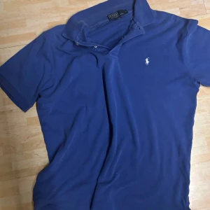 Marinblå pikétröja från Ralph Lauren - Klassisk marinblå pikétröja från Ralph Lauren med vit broderad logga på bröstet. Tröjan har krage, korta ärmar och knäppning framtill. Tillverkad i mjuk bomull som är skön mot huden. Perfekt för en stilren och avslappnad look. Nypris är ca 1800kr mitt pris 600kr❗️❗️ Priset är självklart inte hugget i sten så skicka gärna prisförslag och tveka inte att höra av er vid frågor🙌🏼