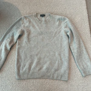 Stickad crew neck från A.P.C. - Snygg ljusgrå tröja från A.P.C. 100% merinoull Rund halsringning och ribbade muddar vid ärmslut och nederkant. På lappen i nacken står det storlek:L men den är i storlek:XS då den har krympt o tvätten. Tröjan är flitigt använd men har inga skador eller liknande. 