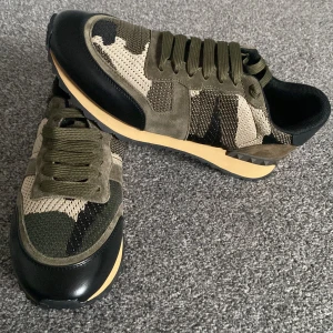 Valentino Garavani Rockrunner sneakers - Snygga Valentino Garavani Rockrunner sneakers i camouflage med olivgröna, beige och svarta toner. Skorna har detaljer i mocka, mesh och skinn, samt coola nitar på hälen. Klassisk snörning och platt sula för en urban vibe. Storlek 43!