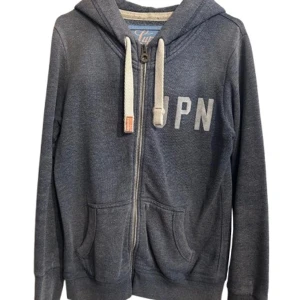 Mörkblå hoodie med dragkedja från superdry(intressekoll) - Mysig mörkblå hoodie från superdry med vita snören, huva och dragkedja framtill. Tryck med bokstäverna JPN på bröstet och två fickor framtill. Perfekt för en chill och avslappnad stil.