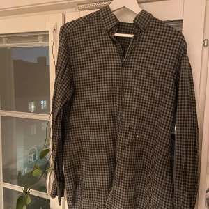 Rutig skjorta från J.Lindeberg - Säljer en snygg rutig skjorta från J.Lindeberg i svart och grått. Skjortan har klassisk krage, knäppning framtill och lång ärm. Perfekt för dig som gillar stilren och enkel design med en modern touch. Hör av er vid minsta fråga.💯