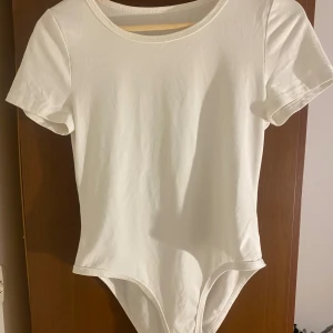 Vit kortärmad body från SHEIN - En basic vit body från SHEIN med rund halsringning och korta ärmar. Gjord i mjuk bomullsmix som sitter skönt mot kroppen. Perfekt att styla med jeans eller kjol för en clean look.