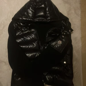 Svart cardigan från Moncler - Säljer en snygg svart cardigan från Moncler. Jackan har en glansig yta med en huva och en broderad Moncler-logga på armen . Perfekt för kyliga dagar när du vill hålla stilen. 🖤
