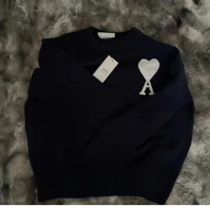 Mörkblå stickad tröja från Ami - Snygg mörkblå stickad tröja från Ami Alexandre Mattiussi med vit hjärtapplikation och bokstaven A på bröstet. Klassisk rund hals och långärmad modell, perfekt för dig som gillar stilrena detaljer och vill ha något som sticker ut lite extra.