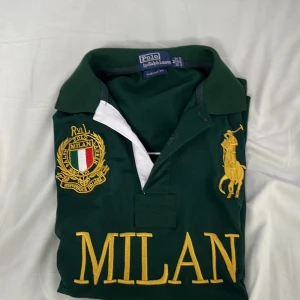 Exclusive Grön pikétröja Polo Ralph Lauren Milan - Säljer en grön pikétröja från Polo Ralph Lauren med stora gula broderier, MILAN-text och italienskt emblem på bröstet. Klassisk krage, vit detalj vid knäppningen och siffra på ärmen. custom fit.