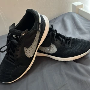 Nike STREETGATO futsal skor - Ett par riktigt fet Joga bonito futsal skor i en svart i vit farkombo. Har ett fantastiskt grepp på planen i o många olika material för maximerad grepp . Säljer för de e för små. Inga slitningar förutom att lite av den blå futsalplanen jag spelade på förut har färgat av sig lite på sulan. Nypris 900
