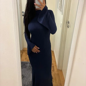 Marinblå ribbad långklänning - Säljer en marinblå långklänning med ribbad struktur och utsvängda ärmar. Klänningen har en figurnära passform och är tillverkad i ett stretchigt material som sitter snyggt på kroppen. Perfekt för dig som gillar stilrena och trendiga plagg.