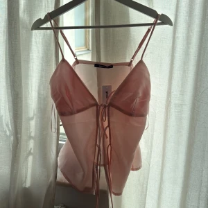 Rosa topp från Gina Tricot - Säljer en ljusrosa, linnetopp från Gina Tricot. Toppen har tunna axelband, snörning framtill och är tillverkad i ett lätt material som ger en luftig känsla. Toppen är helt ny och är storlek 36. 