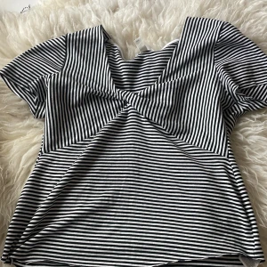 Randig v-ringad topp från H&M Mama - Säljer en svartvit randig topp från H&M Mama i storlek L. Toppen har v-ringning och korta ärmar, med ett snyggt twistat parti framtill. Tillverkad i mjuk bomull som känns skön mot huden. Perfekt för dig som vill ha en bekväm och stilren look.