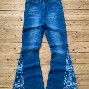 Blå bootcut jeans med paisleydetalj W28 L32 - Snygga blå bootcut jeans från YMI med paisleymönstrade tygkilar i benen. Hög midja och klassisk femficksdesign. Jeansen har råa kanter nertill och cool kontrast mellan denim och mönstrat tyg. Perfekta för dig som vill sticka ut med din stil.  Storlek: W28 L32
