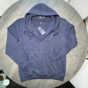 Blå hoodie från Polo Ralph Lauren - Köpte fel storlek ‼️Snygg marinblå hoodie från Polo Ralph Lauren med dragkedja och huva. Tröjan har broderad logga på bröstet, snörning i huvan och två fickor framtill. Tillverkad i mjuk bomull för en skön och avslappnad stil.