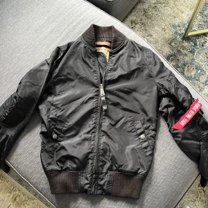 Svart bomberjacka Alpha Industries XS - Säljer en klassisk svart bomberjacka från Alpha Industries i storlek XS. Jackan har orange foder, grov dragkedja, ribbade muddar och den ikoniska röda 'Remove Before Flight'-taggen på ärmen. Tillverkad i slitstark polyester och har två fickor med tryckknapp. Nypris ca 2300kr❤️