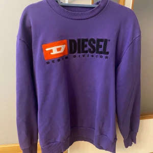 Lila vintage sweatshirt från Diesel, stl S - Cool lila sweatshirt från Diesel med broderad logga i svart och orange framtill. Tröjan har rund hals, ribbade muddar och är tillverkad i mjuk bomull. Perfekt för dig som vill sticka ut med färg och streetstyle.